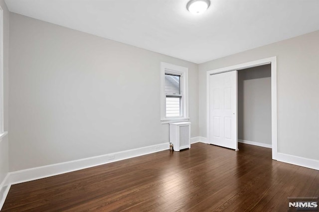 unfurnished bedroom featuring radiator, a closet, and dark hardwood / wood-style flooring