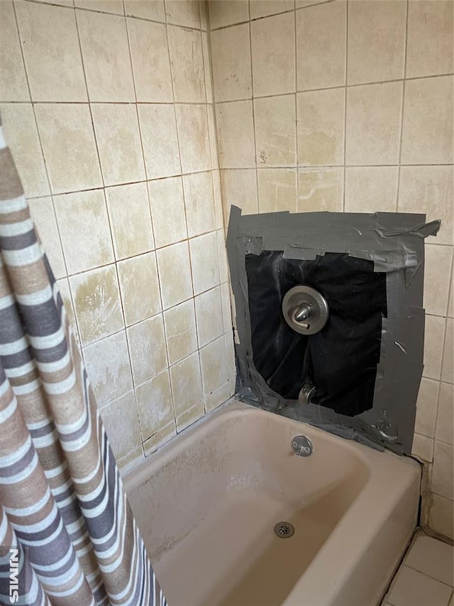 bathroom with a tub to relax in, tile patterned floors, and tile walls