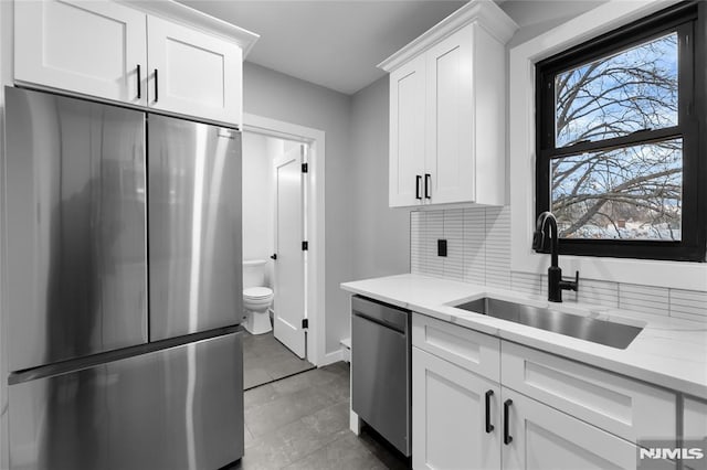 kitchen featuring white cabinetry, sink, stainless steel appliances, light stone counters, and backsplash