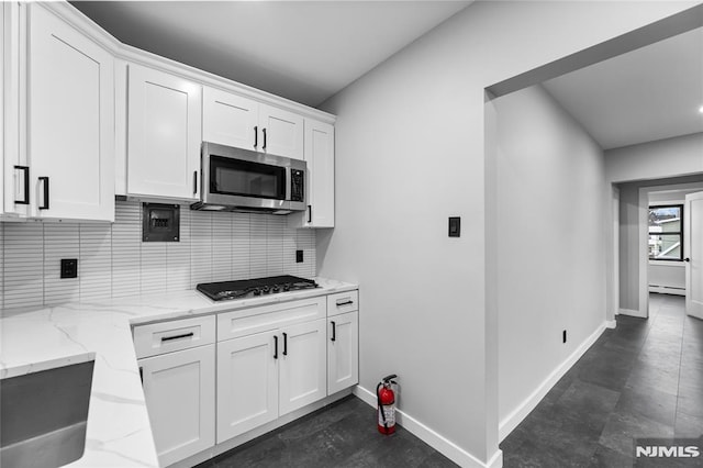 kitchen with backsplash, white cabinetry, light stone countertops, and appliances with stainless steel finishes