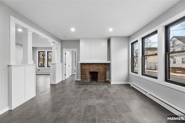 unfurnished living room with ornate columns, a fireplace, and a baseboard heating unit