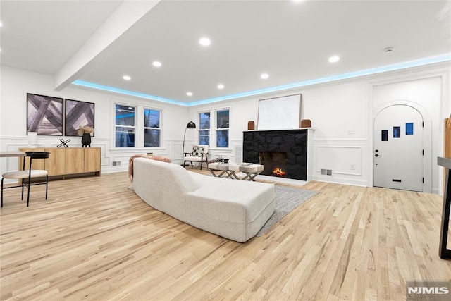 living room with a fireplace, beamed ceiling, and light wood-type flooring