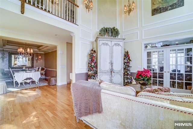 living room featuring wood-type flooring, crown molding, a towering ceiling, and french doors