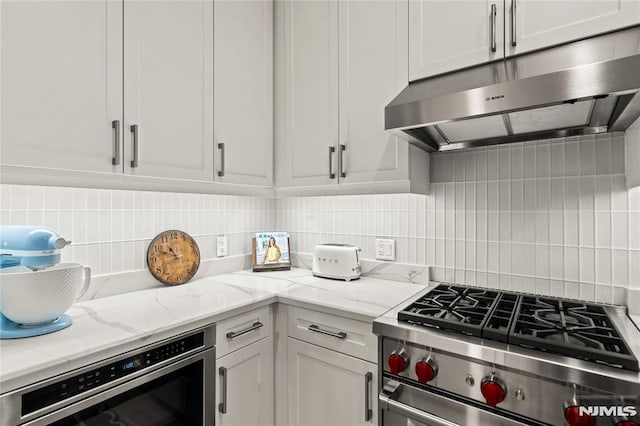 kitchen featuring backsplash, white cabinets, stainless steel stove, light stone countertops, and beverage cooler