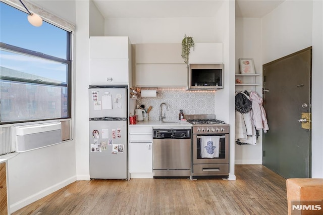 kitchen with sink, white cabinets, light hardwood / wood-style floors, decorative backsplash, and appliances with stainless steel finishes