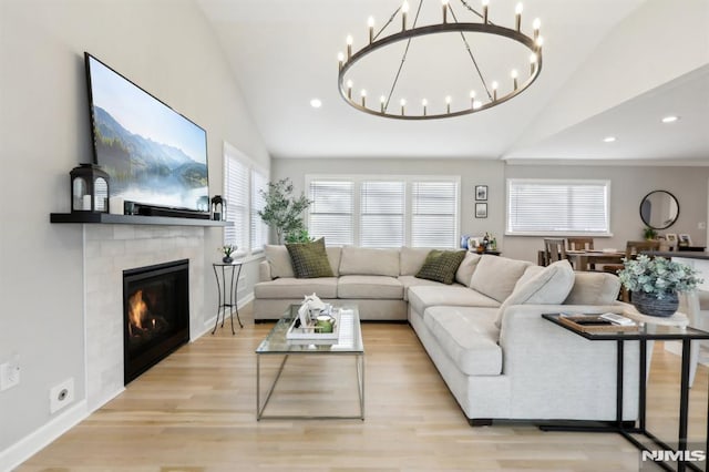 living room with lofted ceiling, a tiled fireplace, light wood-type flooring, and an inviting chandelier