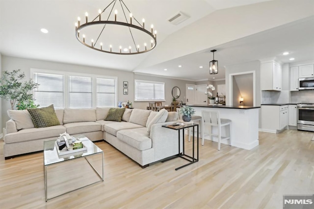 living room with lofted ceiling, a notable chandelier, and light hardwood / wood-style flooring