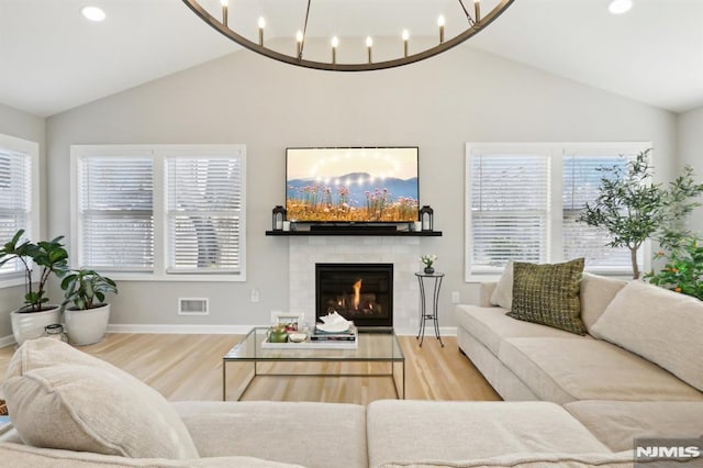 living room featuring lofted ceiling, wood-type flooring, a tile fireplace, and an inviting chandelier