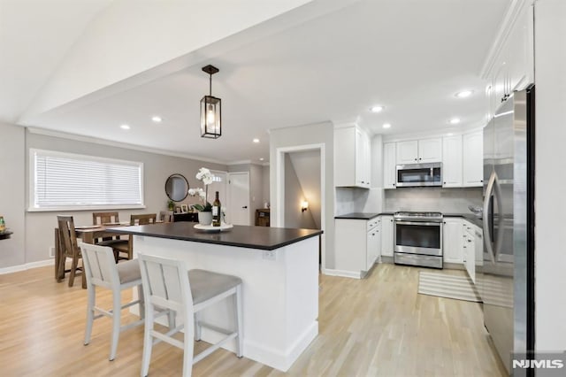 kitchen with decorative light fixtures, a kitchen bar, light wood-type flooring, stainless steel appliances, and white cabinets