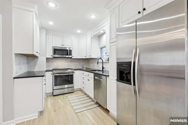 kitchen with backsplash, light hardwood / wood-style floors, sink, white cabinetry, and appliances with stainless steel finishes