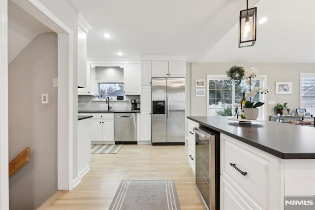 kitchen featuring beverage cooler, white cabinetry, stainless steel appliances, sink, and hanging light fixtures