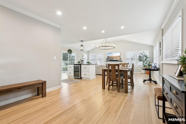 dining area with beverage cooler, lofted ceiling, ornamental molding, a notable chandelier, and light wood-type flooring