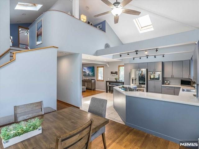 kitchen featuring a skylight, gray cabinetry, ceiling fan, kitchen peninsula, and stainless steel fridge