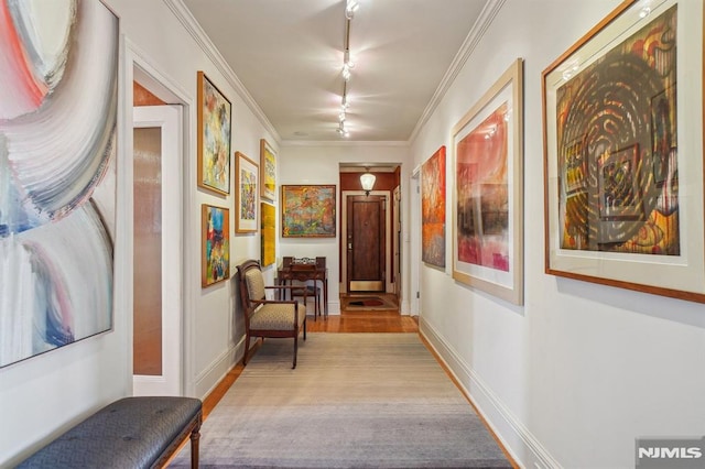 hallway with light wood-type flooring, crown molding, and track lighting