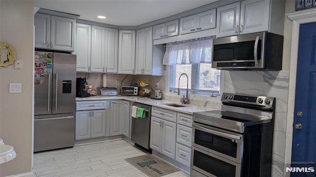 kitchen with decorative backsplash, appliances with stainless steel finishes, light stone countertops, gray cabinetry, and sink