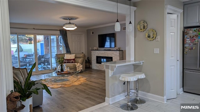 living room featuring a stone fireplace, ornamental molding, and light hardwood / wood-style flooring