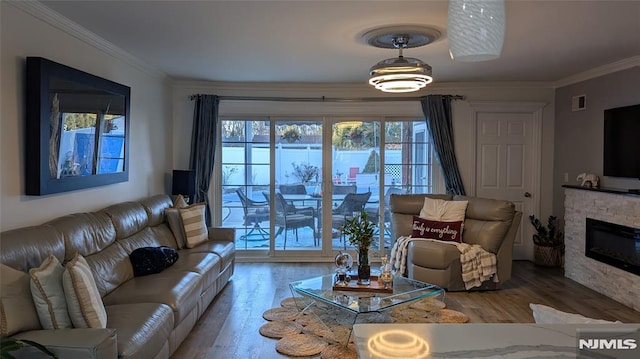 living room featuring a stone fireplace, crown molding, plenty of natural light, and wood-type flooring