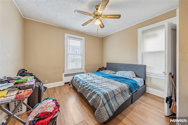 bedroom featuring ceiling fan, radiator heating unit, light hardwood / wood-style floors, a textured ceiling, and ornamental molding