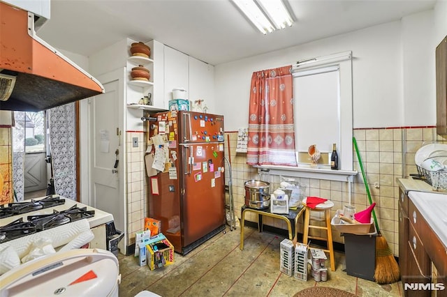 kitchen with refrigerator, gas range gas stove, ventilation hood, tile walls, and white cabinetry