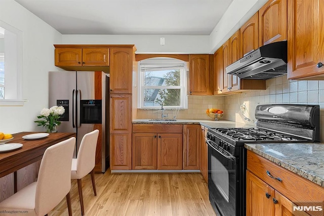 kitchen featuring stainless steel fridge with ice dispenser, light wood-type flooring, black range with gas stovetop, light stone counters, and sink