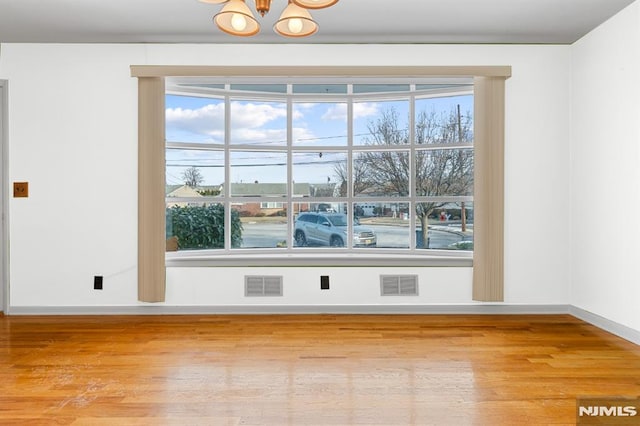 spare room featuring a wealth of natural light, a chandelier, and wood-type flooring