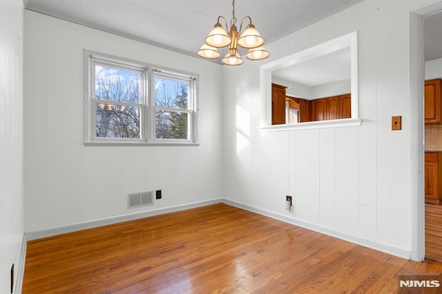 empty room featuring light wood-type flooring and a notable chandelier