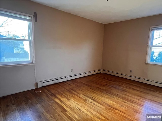 empty room featuring baseboard heating, a wealth of natural light, and hardwood / wood-style flooring