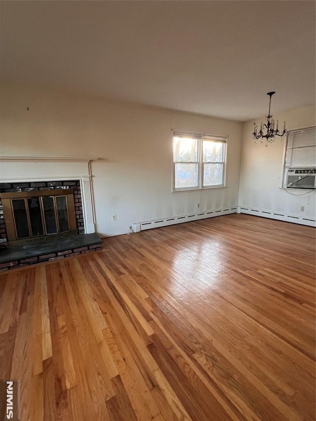 unfurnished living room with a brick fireplace, cooling unit, wood-type flooring, a baseboard radiator, and a chandelier