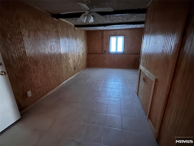 interior space featuring ceiling fan, light tile patterned floors, and wooden walls