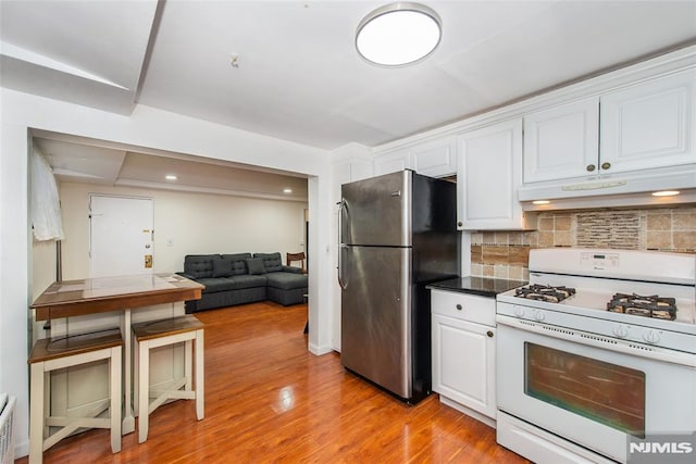 kitchen featuring decorative backsplash, light wood-type flooring, white cabinets, stainless steel refrigerator, and white gas stove