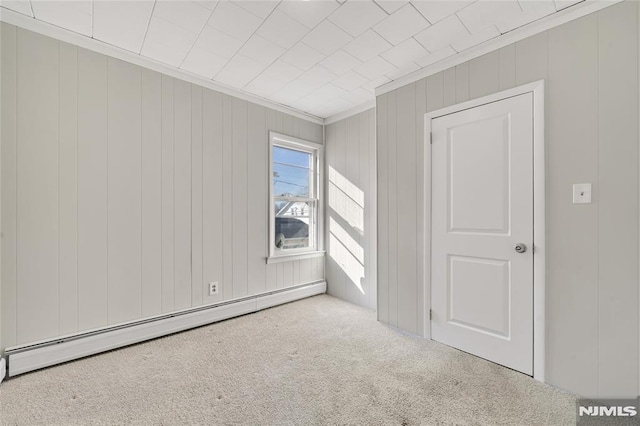 unfurnished room with wooden walls, a baseboard heating unit, ornamental molding, and carpet floors