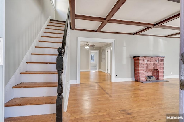 stairs featuring beam ceiling, coffered ceiling, a fireplace, and hardwood / wood-style flooring