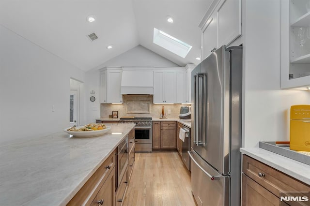 kitchen with backsplash, lofted ceiling with skylight, custom exhaust hood, white cabinetry, and premium appliances