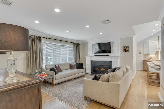 living room featuring light wood-type flooring, ornamental molding, and a fireplace