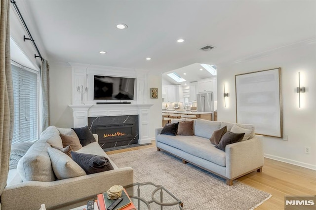 living room with light hardwood / wood-style flooring, ornamental molding, a premium fireplace, and vaulted ceiling