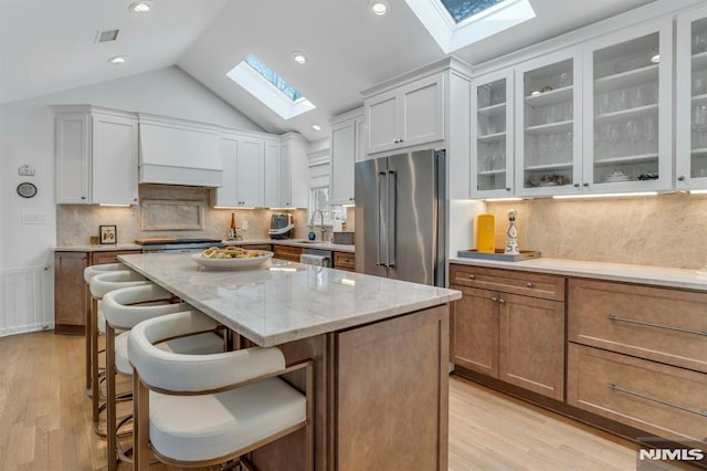 kitchen with white cabinetry, appliances with stainless steel finishes, vaulted ceiling with skylight, a kitchen island, and light stone counters