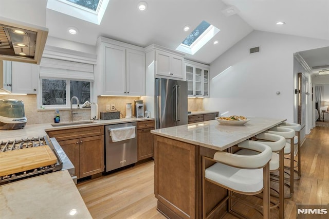 kitchen featuring stainless steel appliances, tasteful backsplash, lofted ceiling with skylight, white cabinets, and sink