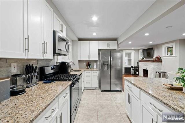 kitchen featuring white cabinets, a fireplace, appliances with stainless steel finishes, light tile patterned flooring, and light stone counters