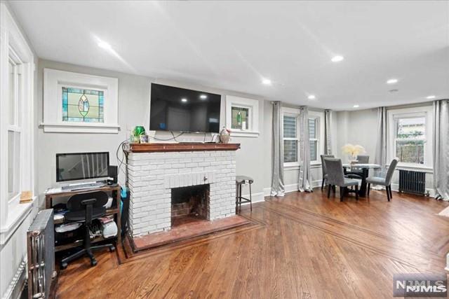 living room with hardwood / wood-style floors, radiator, and a brick fireplace