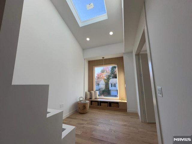 corridor with vaulted ceiling with skylight and light wood-type flooring