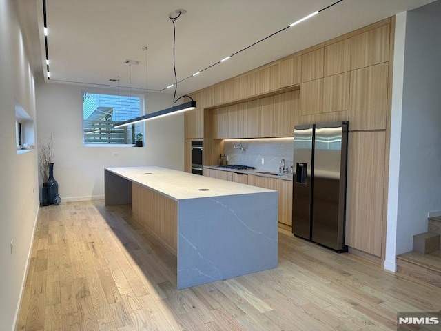 kitchen featuring sink, stainless steel appliances, light hardwood / wood-style flooring, a spacious island, and pendant lighting