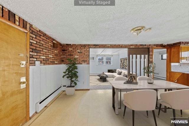 dining room featuring brick wall, a textured ceiling, and a baseboard heating unit