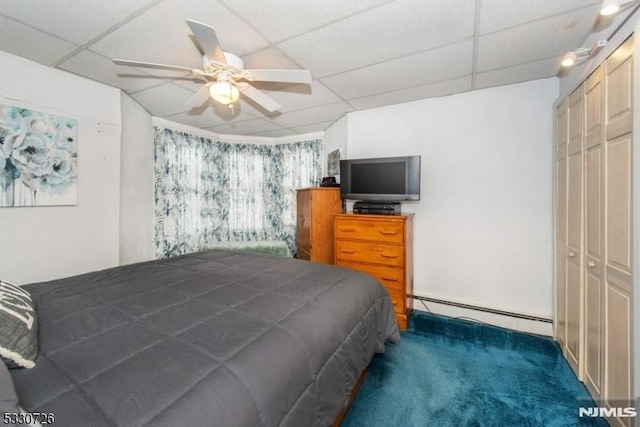 bedroom featuring a drop ceiling, ceiling fan, dark colored carpet, a baseboard radiator, and a closet