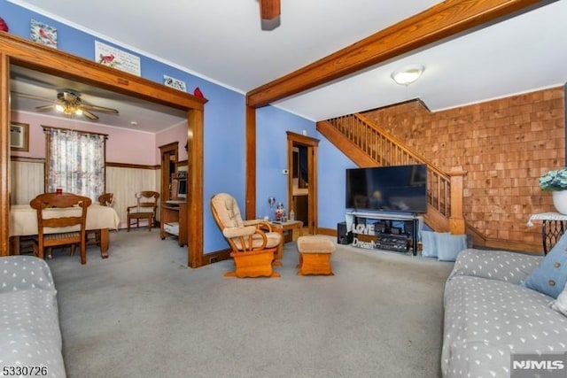 carpeted living room with beamed ceiling, ceiling fan, and wooden walls