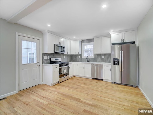 kitchen featuring sink, light wood-type flooring, tasteful backsplash, white cabinetry, and stainless steel appliances