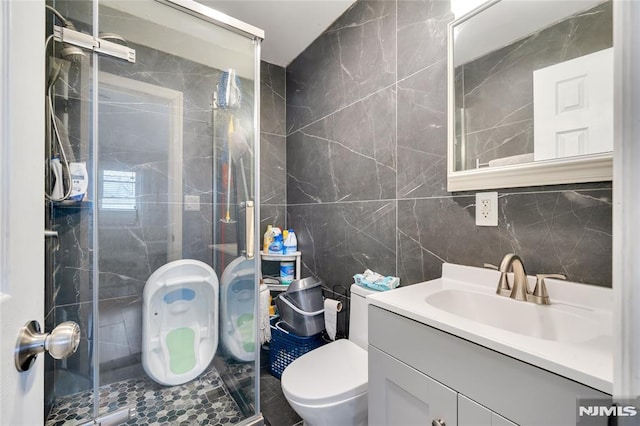 bathroom with walk in shower, vanity, tile walls, and toilet