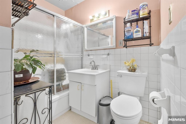 full bathroom featuring vanity, toilet, tile walls, and bath / shower combo with glass door