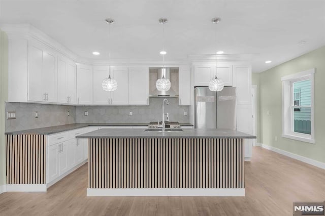 kitchen with stainless steel refrigerator, white cabinets, an island with sink, and wall chimney exhaust hood