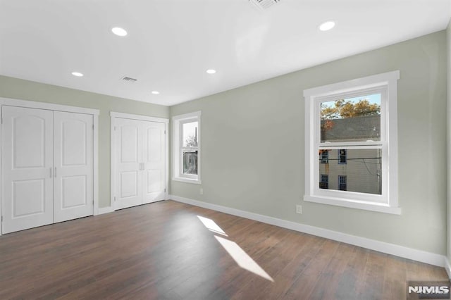 unfurnished bedroom featuring dark hardwood / wood-style floors and two closets