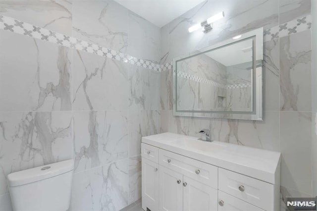 bathroom with vanity, toilet, and tile walls